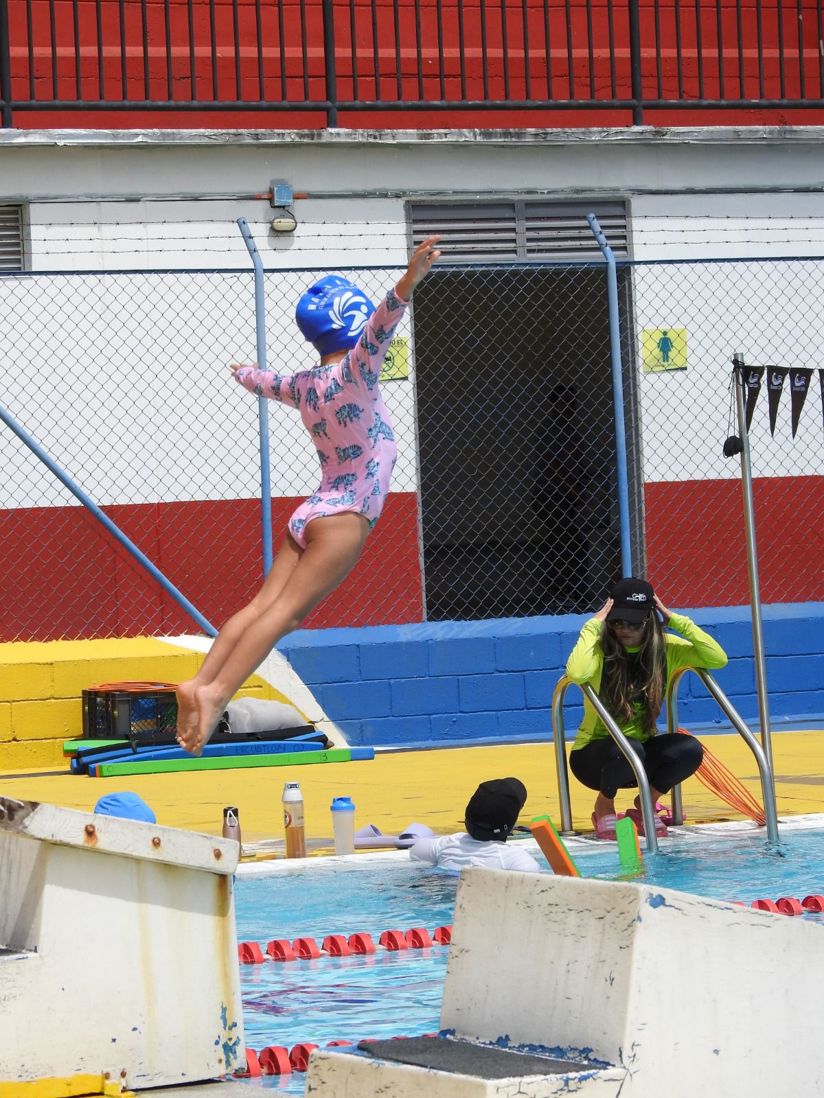 Niña realizando un clavado supervisada por la entrenadora